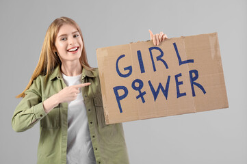 Beautiful young happy woman pointing at paper with text GIRL POWER on grey background. Women...