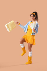 Fashionable African-American woman with bouquet of flowers and shopping bag on beige background. International Women's Day celebration