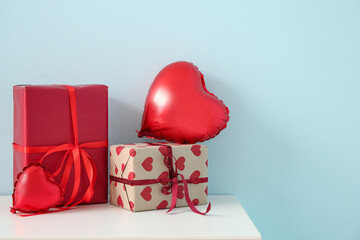 White cabinet with heart-shaped balloons and gift boxes near blue wall. Valentine's Day celebration