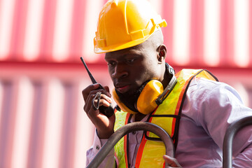 Close up of African American male container yard worker working, control container boxes on forklift truck before loading at commercial dock site. Black male people worker work at cargo freight ship