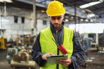 Warehouse workers wear helmets Surrounded by industrial and construction elements. Demonstrate safety, hard work and use tablet to check machine data