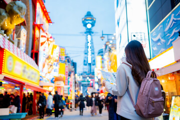 Asian female tourist Traveling and having fun. And she was taking photo with a cell phone camera at Night street with many restaurant around Tsutenkaku Tower in Shinsekai district of Osaka, Japan.