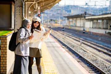 woman girl tourist Two Asian friends but different religions,They were looking at information about preparing to board the train at the train station,She is traveling in Japan. with fun, Japan travel 