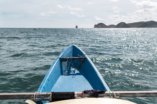 View from the bow of a blue boat with distant rocky islets on the horizon under a bright sky, Indonesia, Asia