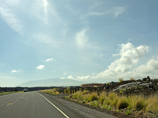 Fototapeta premium Driving to distant Mauna Kea volcano by Saddle road with black volcanic rock landscape and lava shelter on roadside on beautiful sunny day, Big Island of Hawaii