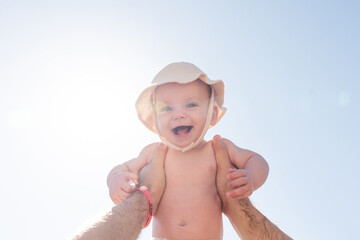 Sun flare highlights a father's hand holding his child aloft. Concept of care and protection in parenthood