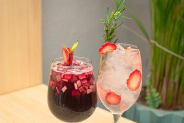 Dos copas una ve cericot con frutas estilo ponche y otra de mojito de frutos rojos sobre una mesa de madera imagen horizontal