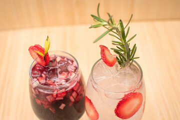 Imagen superior de dos copas de alcohol con hielos una de clericot y mojito de frutos rojos decorado con fresas en la parte superior 