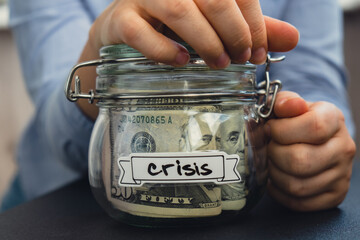 Unrecognizable woman holding Saving Money In Glass Jar filled with Dollars banknotes. CRISIS...