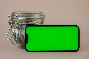horizontal Green screen on modern mobile phone in background of glass jar full of American currency...