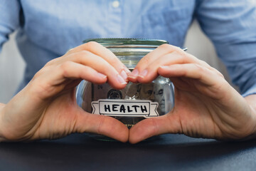 Female showing heart with hands sign Saving Money In Glass Jar filled with Dollars banknotes....
