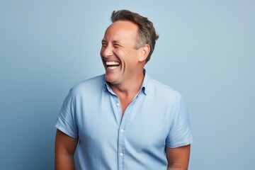 Handsome middle-aged man in blue shirt laughing against blue background