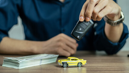 Closeup hand giving a car key and money for loan credit financial and rental. car loan concept, trade car for cash concept, finance concept. Buying or selling new or used vehicle. Car keys on table.