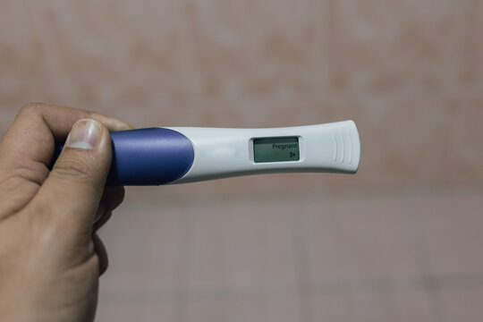 A close-up image of a woman's hands tenderly cradling a positive home pregnancy test