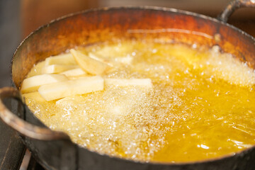 A pan with oil frying sliced potatoes