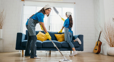 In messy living room two women in uniforms work cleaning employees. With gloves on they tackle dust and dirt on furniture sofas and floors. routine is house care and hygiene. agency small business