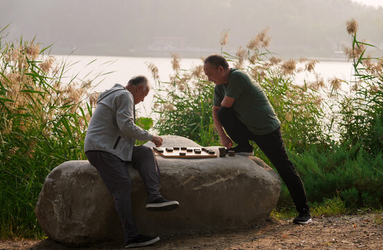 Old people in the park play chess by the lake
