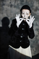 Dramatic vertical portrait of female mime artist standing on stage in spotlight during silent...