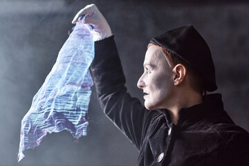 Dramatic side view portrait of mime artist performing on stage and holding shimmering cloth to light, copy space