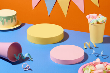 Two cylindrical platforms are displayed on a blue surface with paper cups, ribbons and...