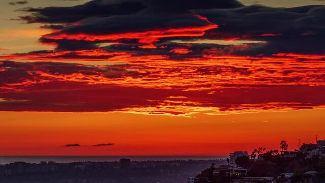 Epic red sunset clouds moving over the ocean and city of Los Angeles and Hollywood Hills skyline silhouette. 4K timelapse.