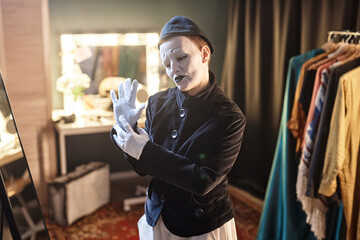 Waist up portrait of female mime performer dressing in costume backstage preparing for show