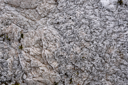 The texture of the stone cliffs covered with frost with snow. Rough aged granite stone frost covered surface.
