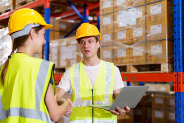 Caucasian male and female warehouse personnel engage in amicable conversation, culminating in a cordial handshake.