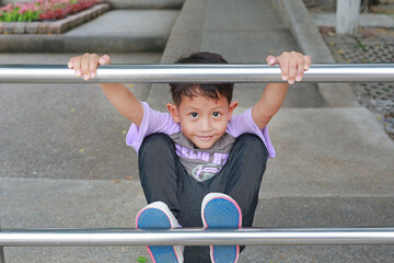 Fototapeta premium Asian little boy kid having fun to climbing aluminum fence in public park.