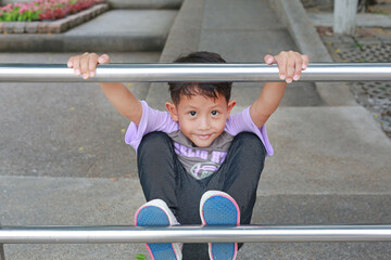 Asian little boy kid having fun to climbing aluminum fence in public park.