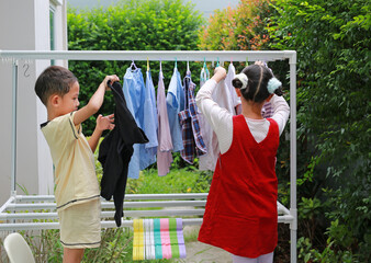 Portrait of Asian girl and boy helping to do dry the clothes at garden near house. Sister and...