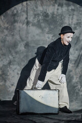 Vertical full length portrait of mime artist performing act with suitcase on stage in spotlight