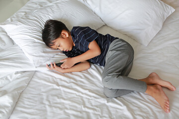 Portrait of Asian little boy playing a smartphone while lying on bed at morning.