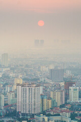 Aerial view of a city skyline with a golden Sun setting into haze over Hanoi in Vietnam