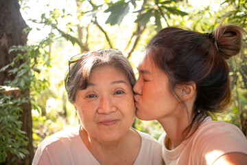 Close up of Happy asian Thai Chinese daughter kissing her elder mother cheek, while relaxing sitting and drinking at cafe in garden.