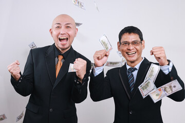 Two Asian successful businessmen throwing out money banknotes while clenching fist 