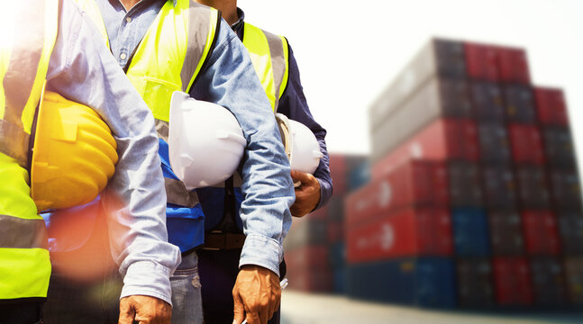 Multiethnic team male Engineer maintenance department site work container service : Group of male workers wearing safety vests and holding helmets outdoor container loading yard meeting teamwork.