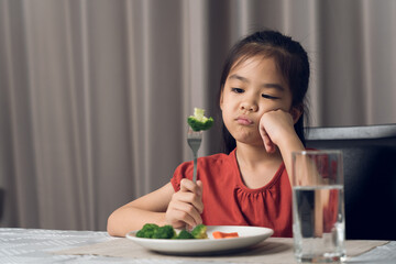 Little cute kid girl refusing to eat healthy vegetables. Children do not like to eat vegetables.