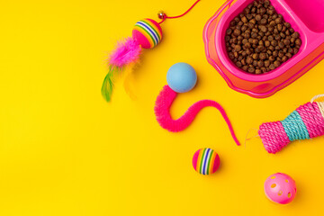 Cat bowl with dry food and toys on yellow background studio shot