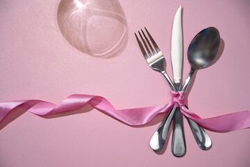 Silverware of fork, knife, and spoon tied up on pink ribbon