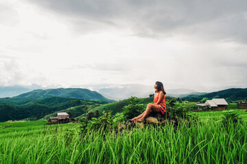 Fototapeta na wymiar Beautiful Asian woman feel relaxing and enjoying in in the meadow. Green rice seedlings in a paddy field with beautiful sky and cloud. Ban Pa Bong Piang, Chiangmai Province, Thailand.