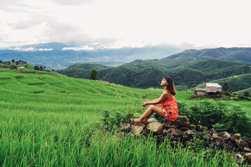 Beautiful Asian woman feel relaxing and enjoying in in the meadow. Green rice seedlings in a paddy field with beautiful sky and cloud. Ban Pa Bong Piang, Chiangmai Province, Thailand.