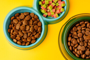 Bowl with dry pet food on yellow background studio shot