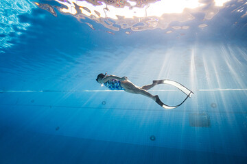Beauty freediver Asian women diver with fins glides underwater in transparent blue pool. Freediver...