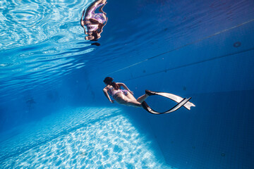 Beauty freediver Asian women diver with fins glides underwater in transparent blue pool. Freediver...