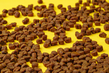 Dry cat food scattered on yellow background studio shot