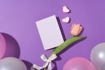 Heart-shaped marshmallows, tulips and decorative balloons on a purple background. A white card for a birthday wish design. Special present. Copy space.