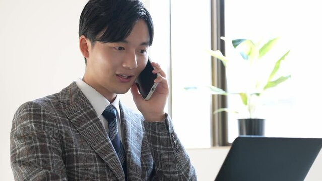 携帯で話しながらパソコンを見る若い男性