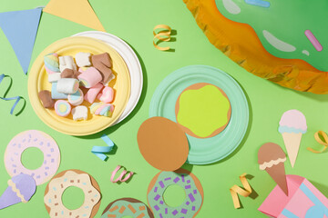 Marshmallows on a round plate, donuts and ice cream made from colored paper, ribbons and cute decorations on a pastel green background. Copy space with flat lay.