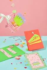 The background is divided into pastel pink and blue. Happy birthday cards with cute drawings. Colorful gummy candies and confetti are decorated on the background.